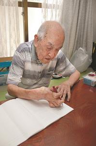 曲がったままの右指でペンを握る平田健二さん＝7月、東京都江東区の写真